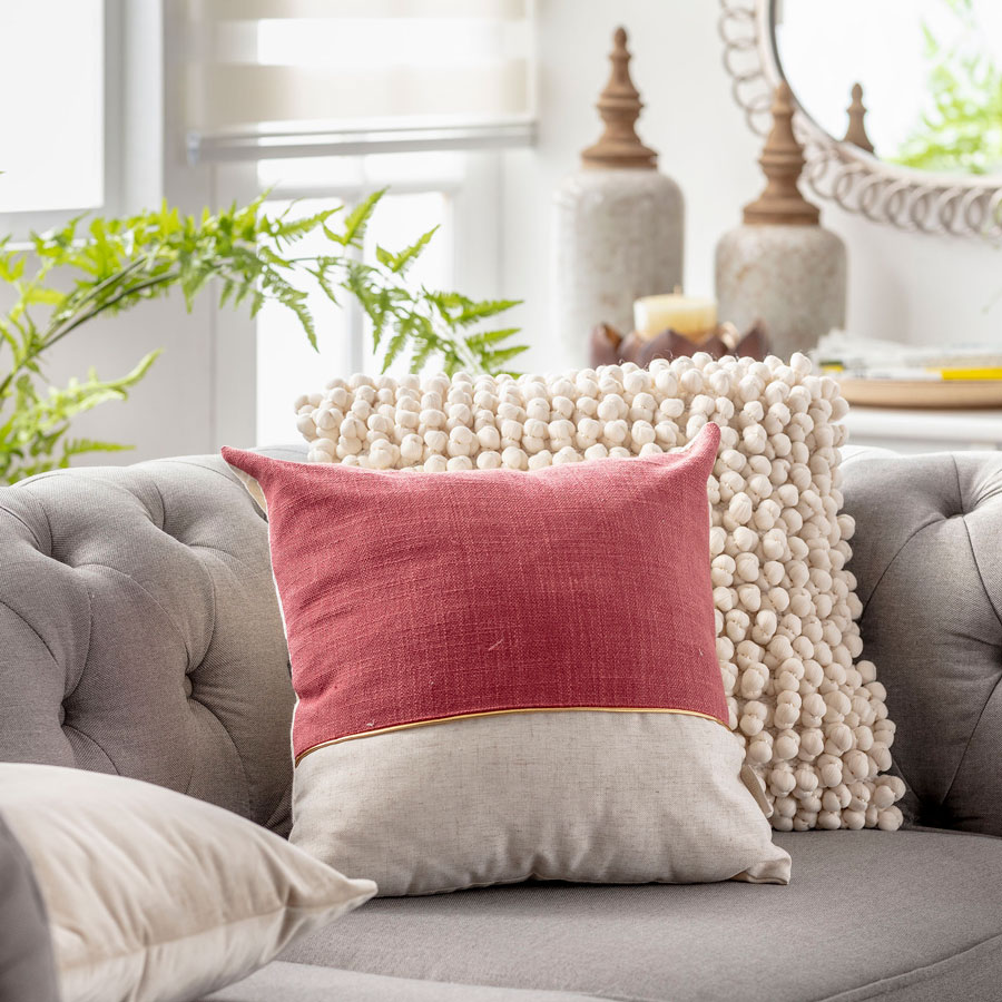 Sofa gris con cojin en tonos rojos y cojin de bolitas de lana