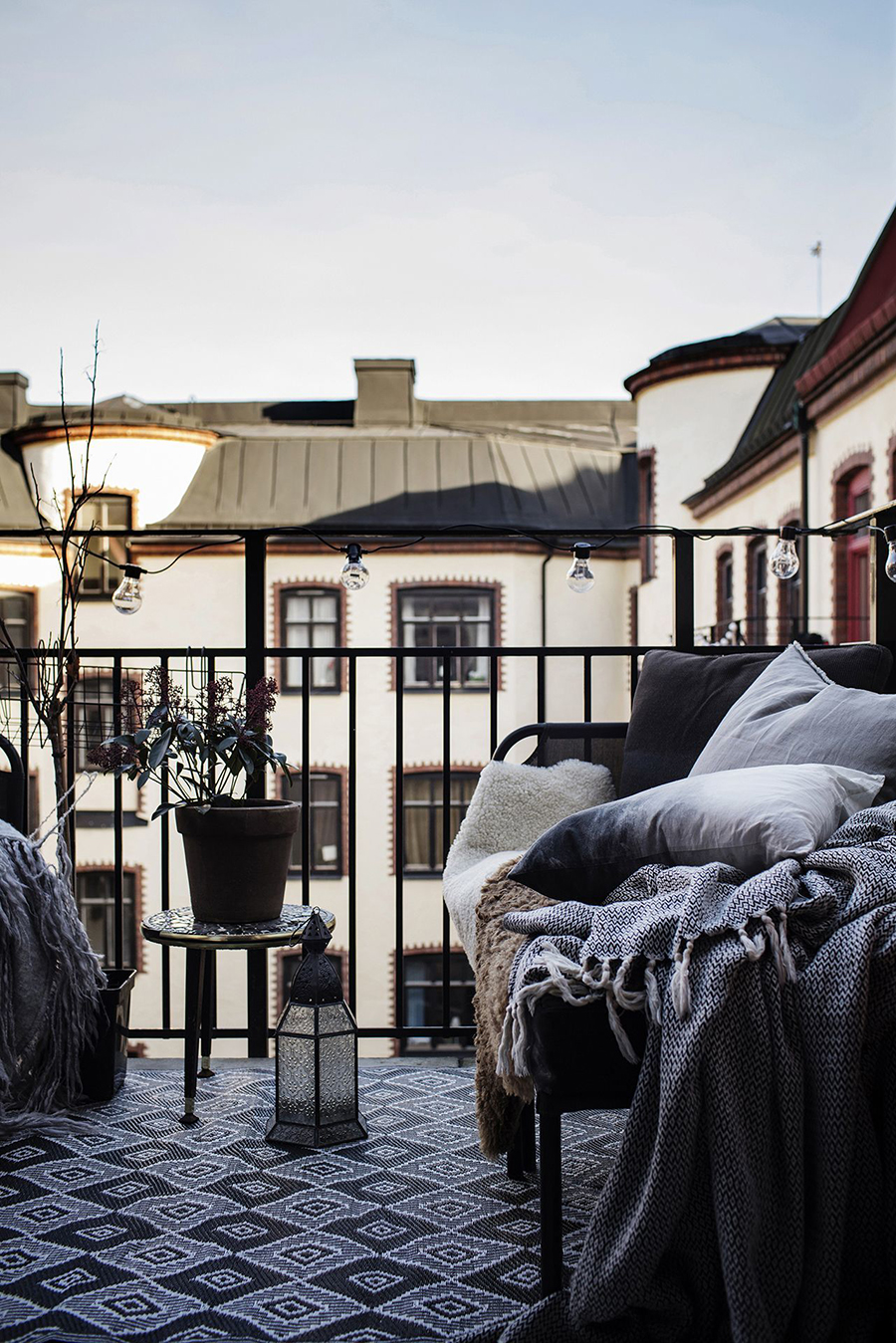 Balcón con muebles de fierro negros. Una mesita con una planta y un sofá con textiles.