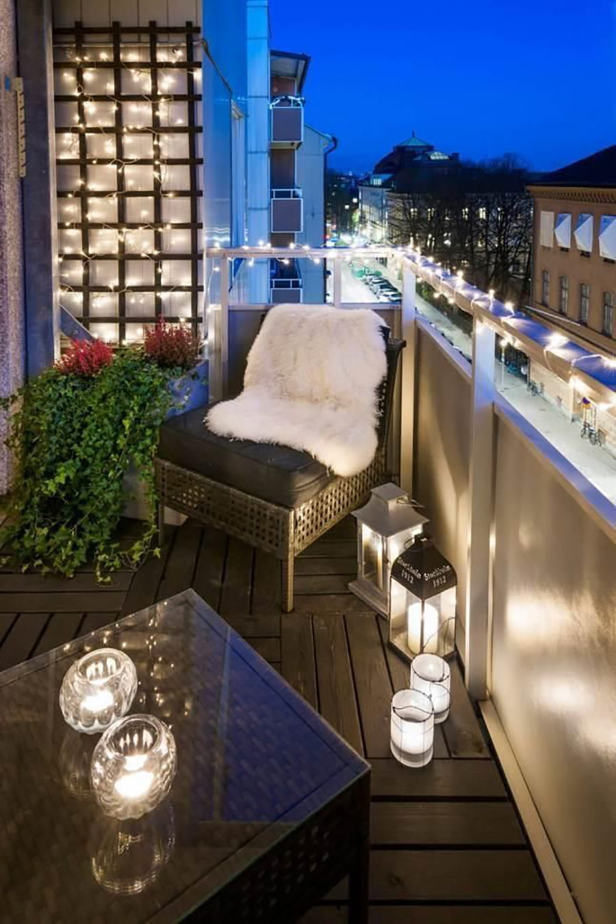 Un balcón con tiras de luces led y fanales. Completan la iluminación velas sobre la mesa y en el piso.