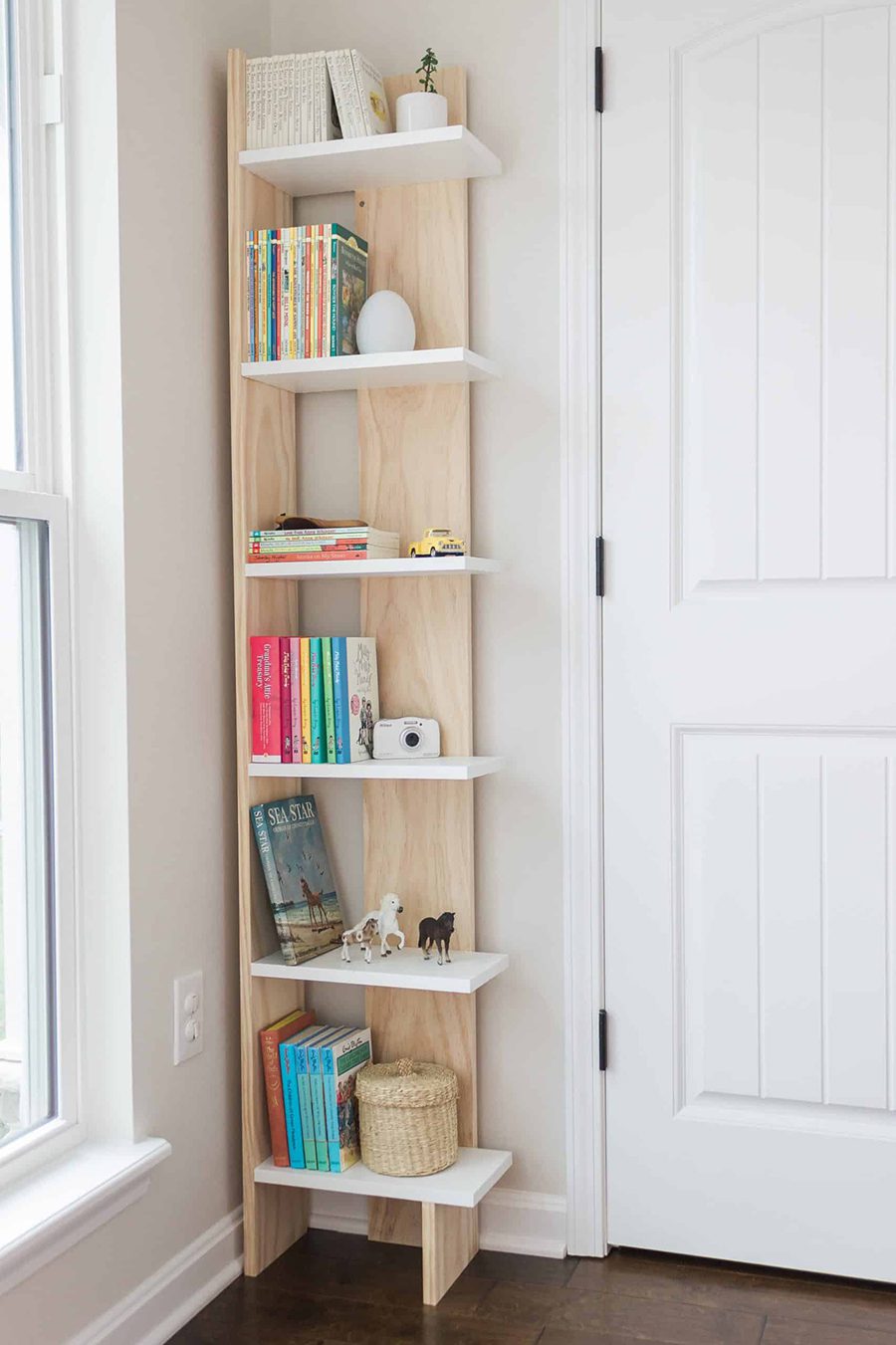 Una estantería de madera para poner en la esquina, con borde por un lado, para que los libros que se encuentran sobre ella en la fotografía tengan tope y no se caigan.