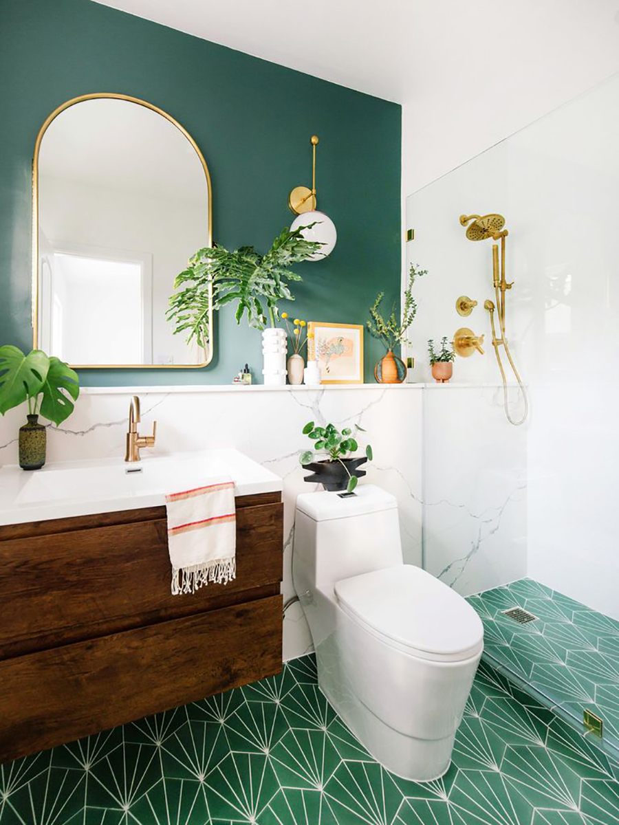 Un baño decorado con estilo vintage moderno, con toques dorado y plantas que combinan con el muro y piso verde.