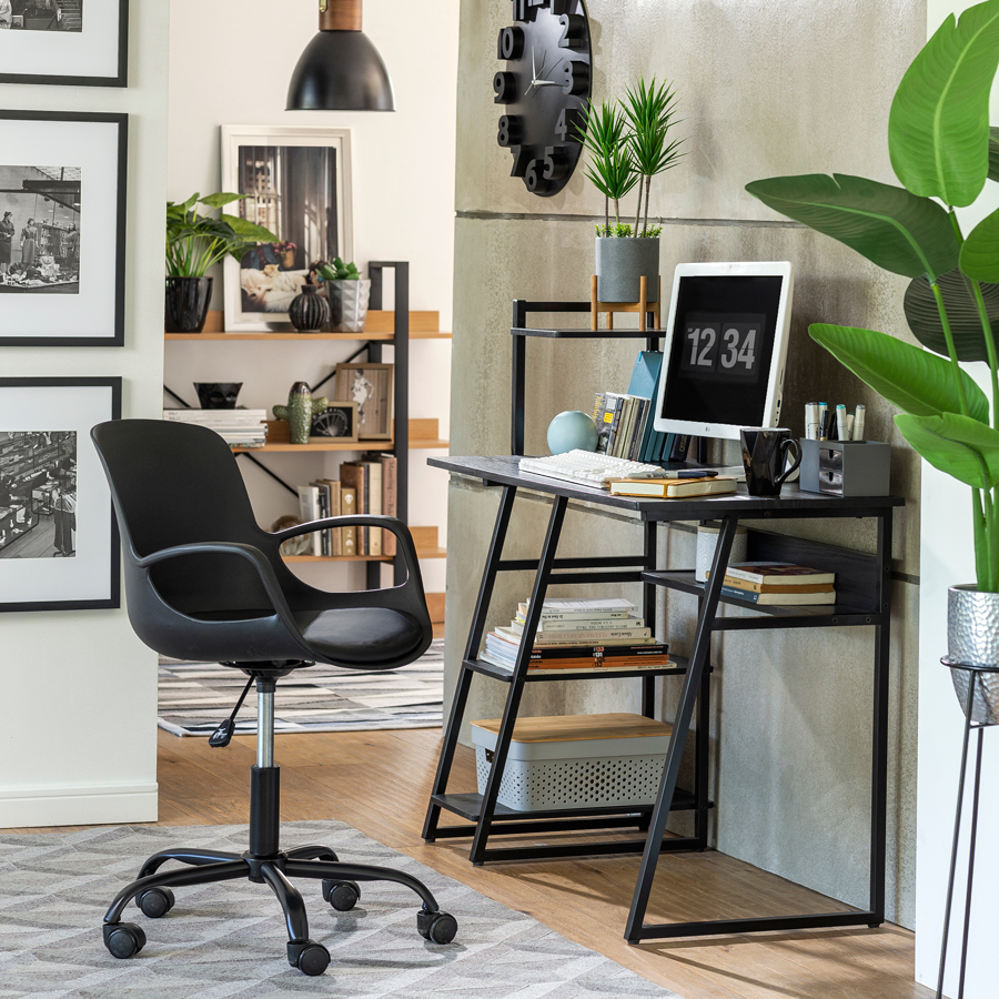 Escritorio ejecutivo urbano de metal en color negro, acompañado de una silla negra. Como elementos decorativos hay un reloj de pared análogo negro, plantas artificiales y cuadros con fotos en blanco y negro.