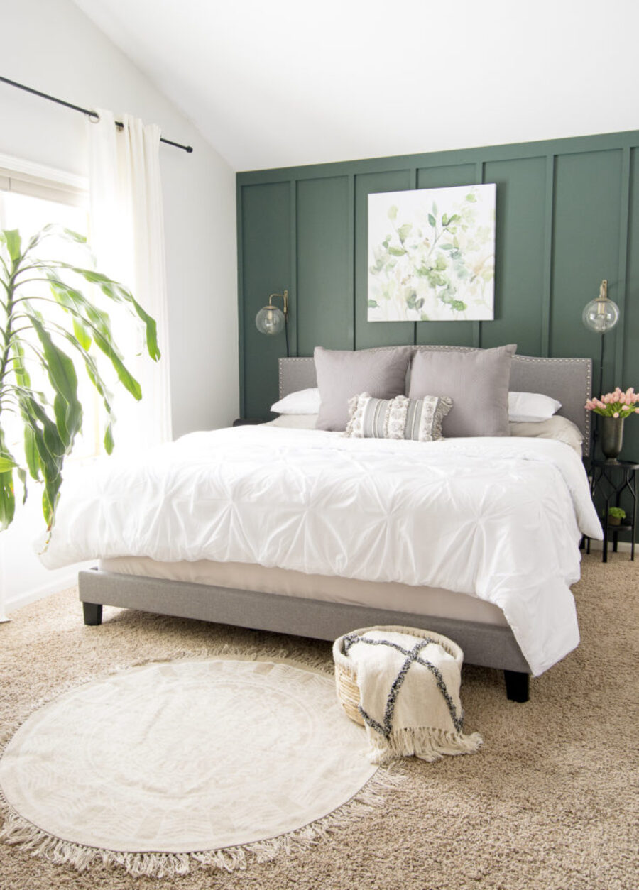 Dormitorio con alfombra beige, techo blanco y una pared de acento verde oscuro. La cama tiene un respaldo y cojines grises, cobertor blanco y sábanas beige. 