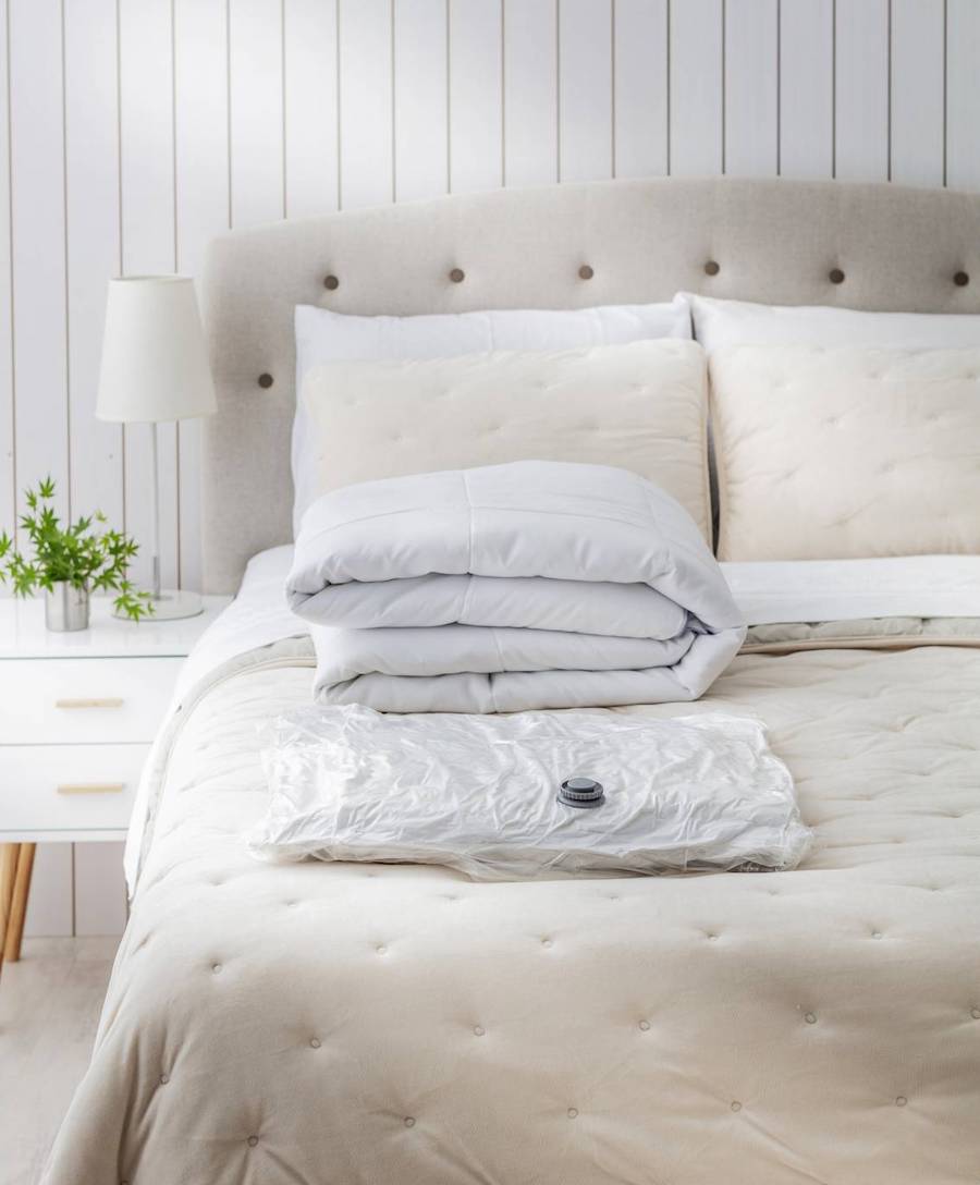 Dormitorio en tonos blancos y crema. Sobre la cama hay un plumón blanco doblado y a su lado, una bolsa de almacenaje al vacío con otro plumón en su interior.
