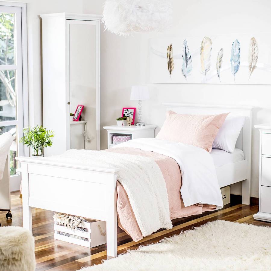 Dormitorio de muros y muebles blancos, suelo de madera y alfombra blanca y peluda. Junto al velador hay un mueble zapatero blanco con una puerta con espejo.
