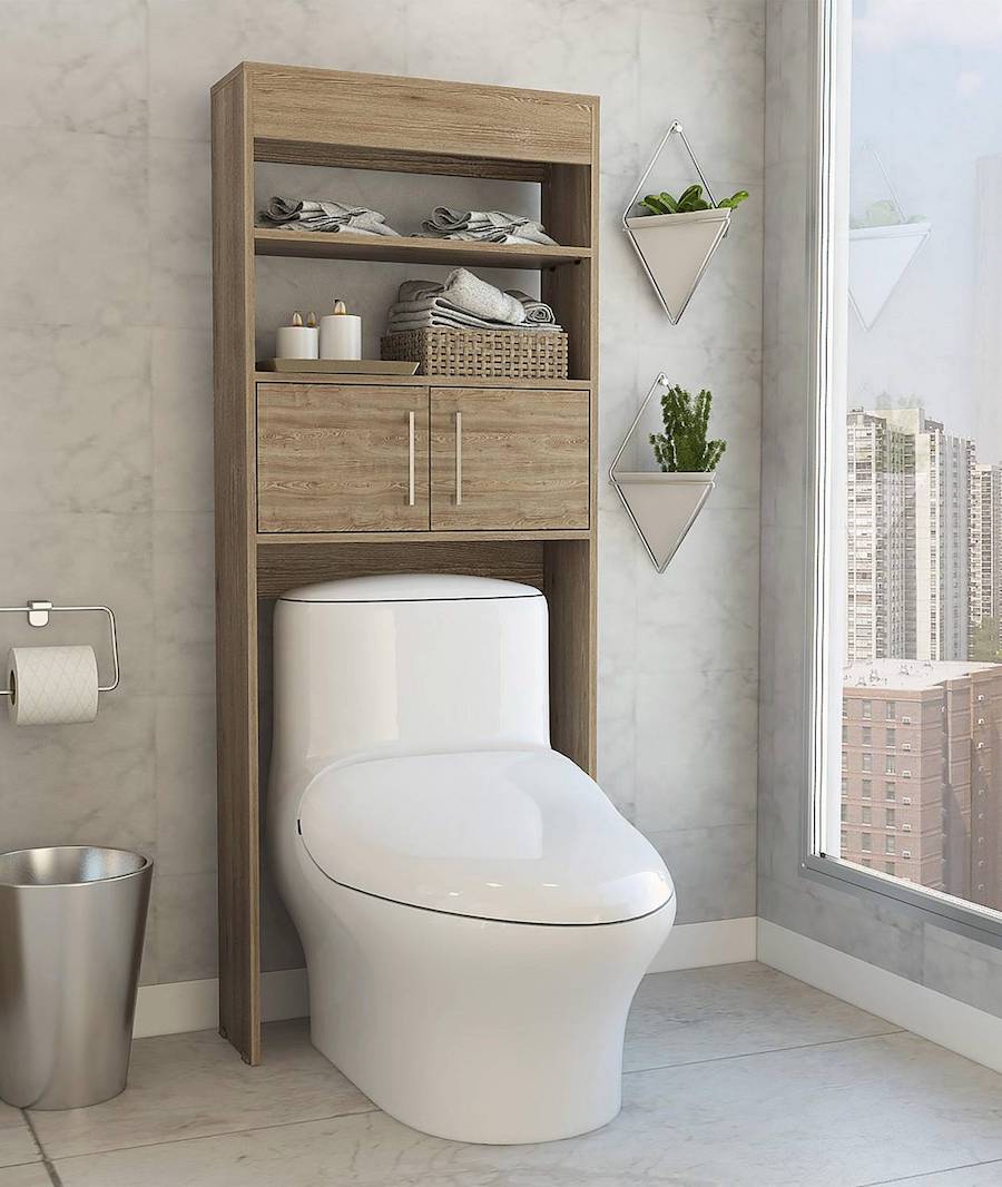 Mueble de baño de madera sobre un WC blanco. El mueble tiene dos repisas y un espacio con dos puertas pequeñas. Sobre las repisas hay toallas y una velas artificiales. A su costado hay unas plantas colgantes.